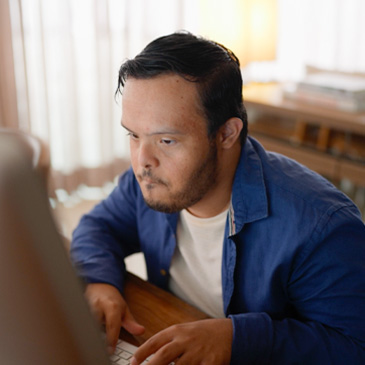 Photo of a person in blue shirt typing at a desk in a room with curtains