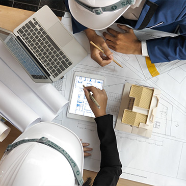 Photo of engineers reviewing building plans with blueprints, a laptop, and a model on a table