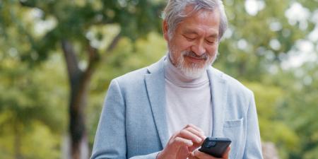 Photo of senior man smiling while using his phone in a park