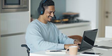 Photo of man wearing headphones, smiling while using a laptop at home