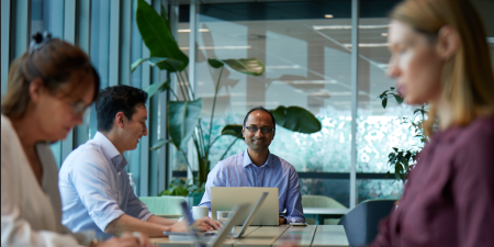 Photo of people in a modern office meeting around a conference table with laptops and notes