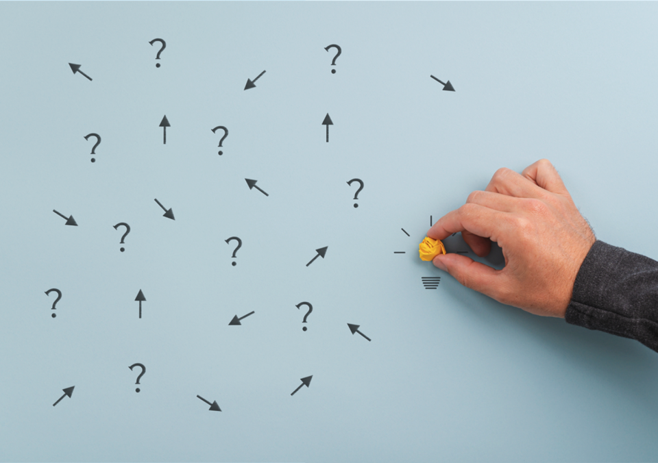 Photo of hand holding a crumpled yellow paper ball with question marks and arrows on a blue background