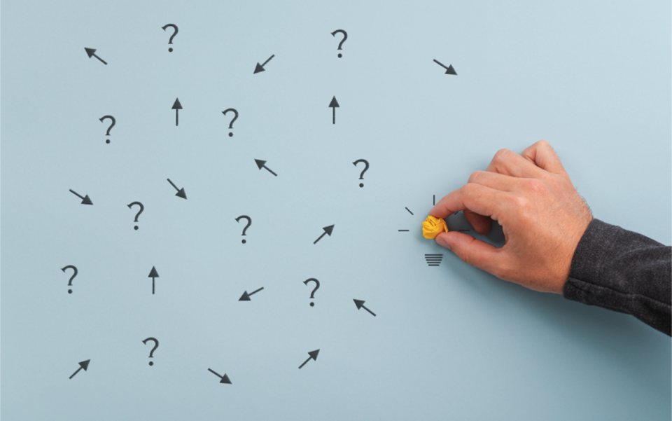 Hand holding a yellow paper lightbulb among question marks and arrows | Test and Buy Innovation | Digital NSW