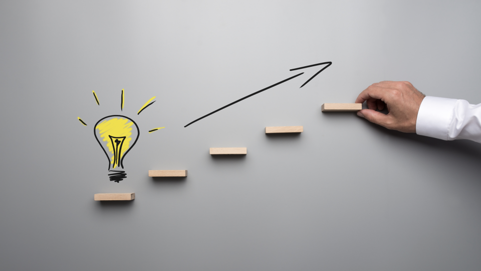 Hand placing steps toward innovation with light bulb and arrow | Test and Buy Innovation | Digital NSW