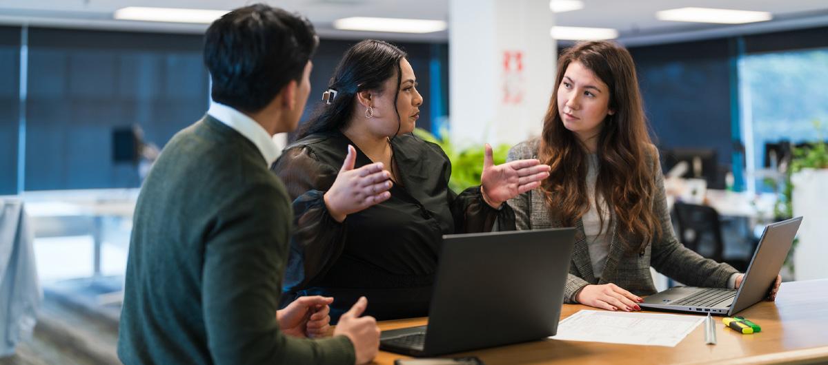 Photo of three people discussing around a table with laptops in an office