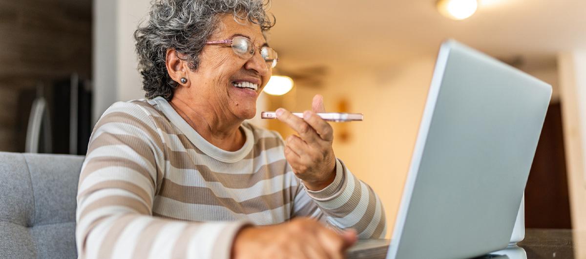 A photo of an elderly woman talking on a mobile phone while using a laptop at a desk