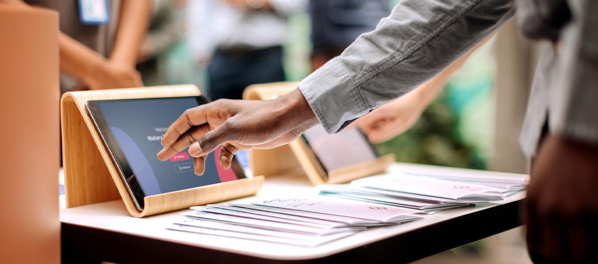 Photo of a person using a tablet at an event registration desk with pamphlets