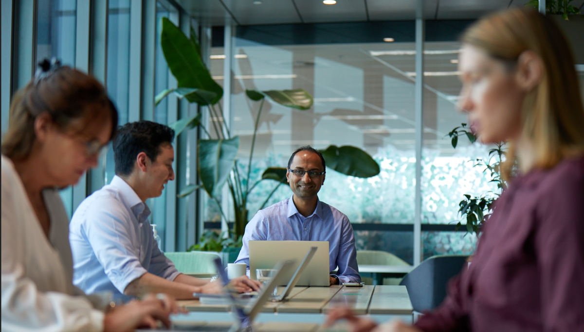 Photo of people in a modern office meeting around a conference table with laptops and notes