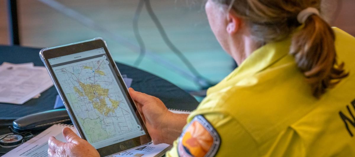 Photo of a person in yellow uniform reviewing a map on a tablet at a table with documents