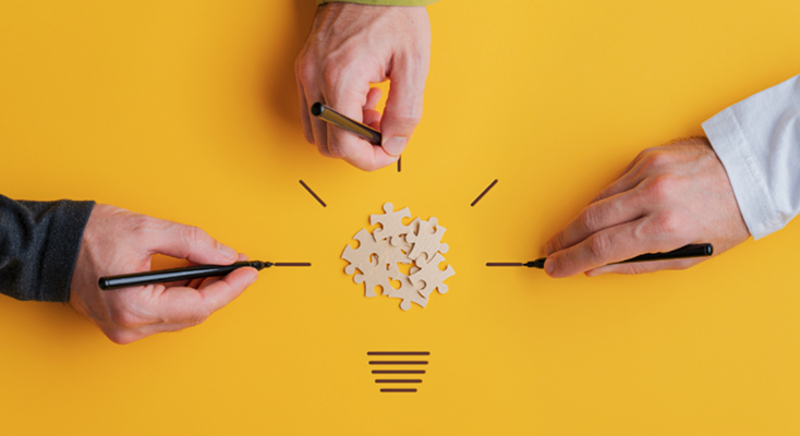 Hands with pens around puzzle pieces shaped like a light bulb | Test and Buy Innovation | Digital NSW