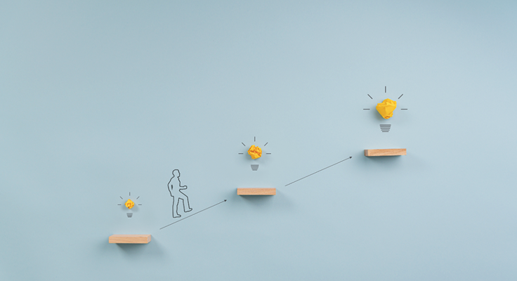 Photo of a line drawing of a person climbing wooden steps with crumpled paper light bulbs, symbolising idea development and progress