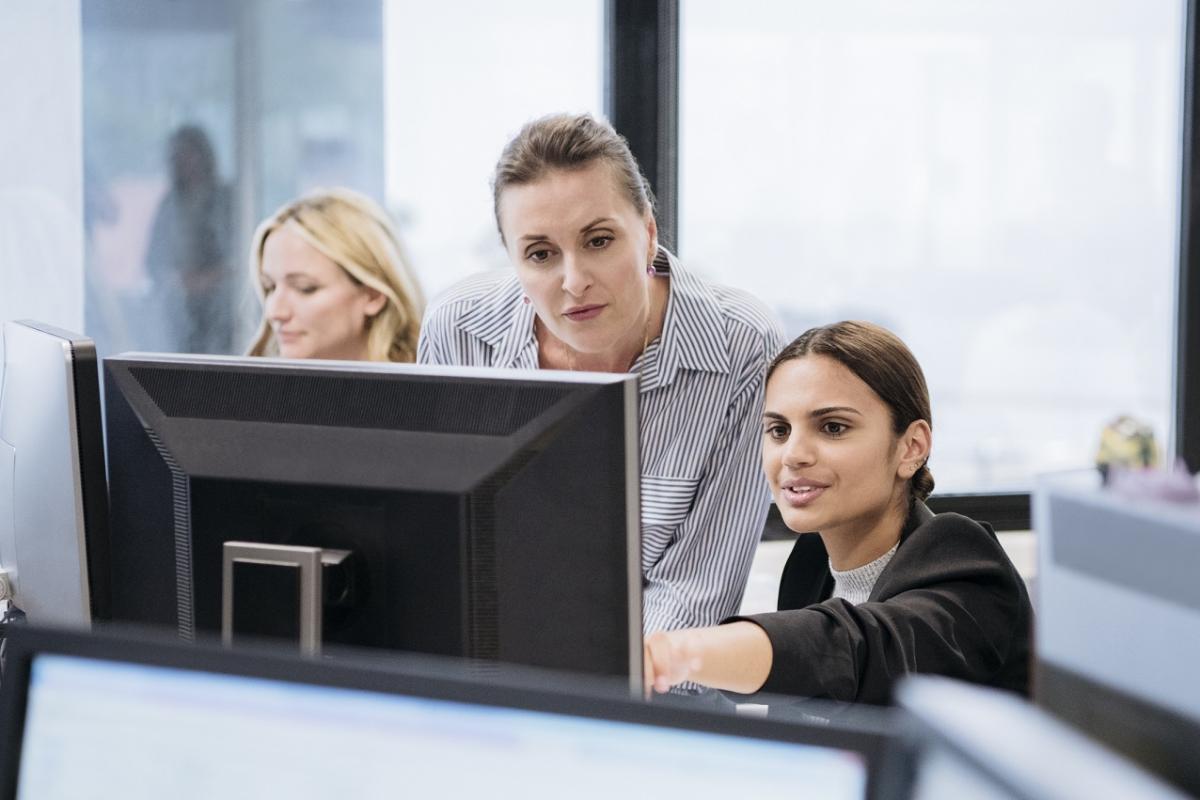 NSW office. Women at work using computer, young woman pointing to screen, mid adult woman watching